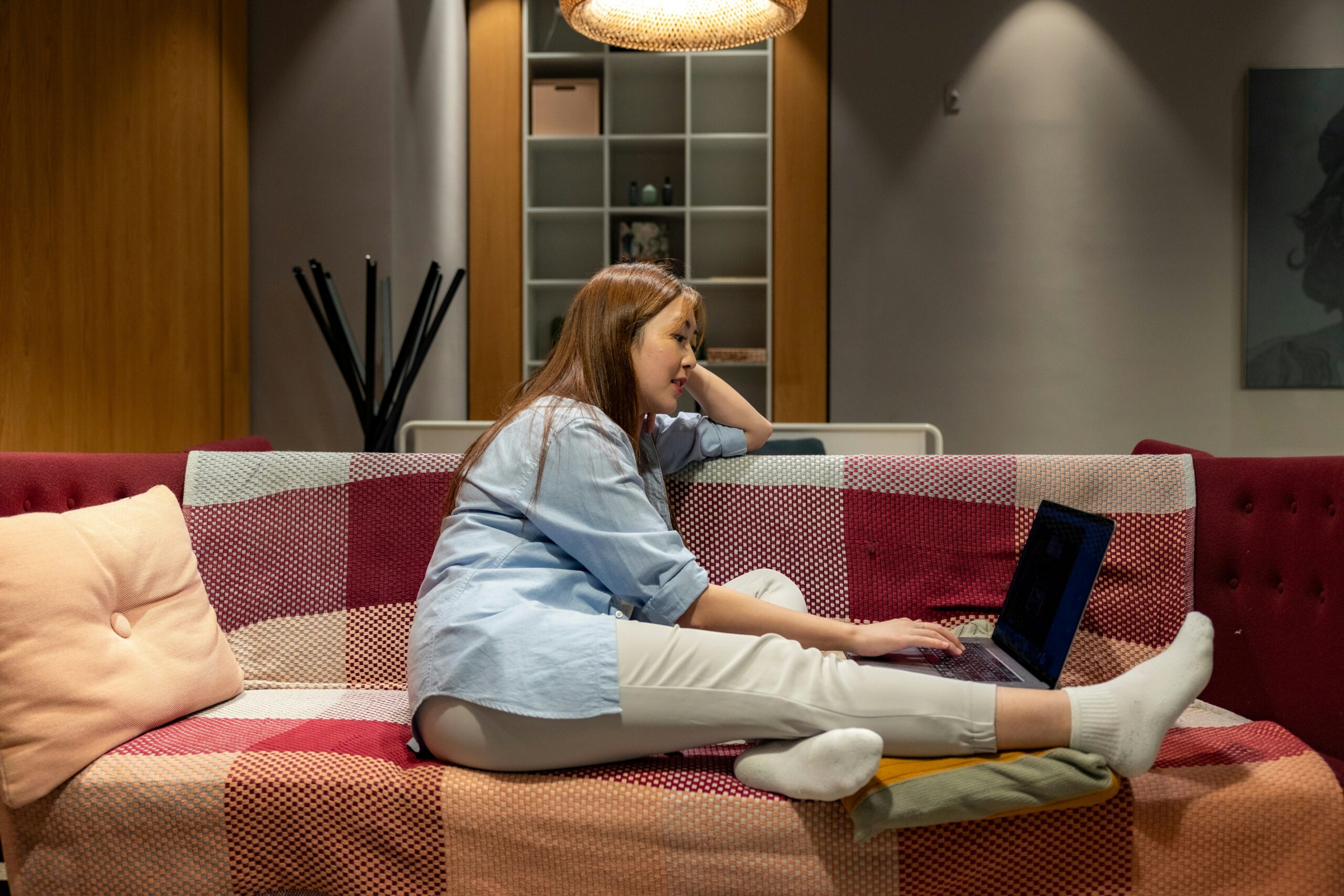 A young woman looks at her laptop as she attends an online nutrition counseling session from her sofa.