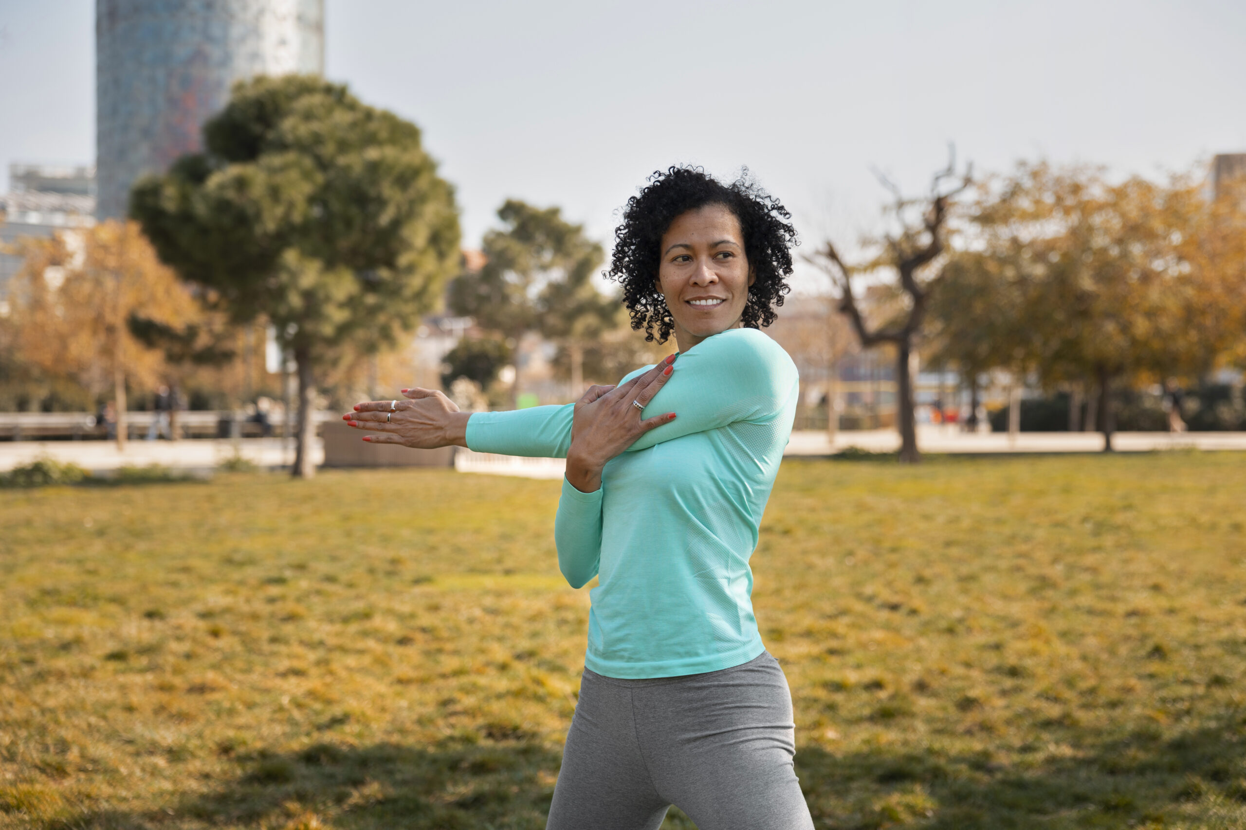 A woman smiles as she stretches in a city park before a run.